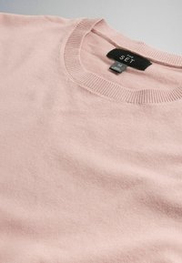 Hellrosa Rundhals-Pullover flach ausgelegt, zeigt gerippten Halsausschnitt und Größenschild mit der Aufschrift „The Set, M.“