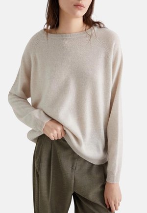 Maglione beige chiaro a pullover con vestibilità rilassata, polsini a coste e texture morbida, abbinato a pantaloni verde oliva per un contrasto.