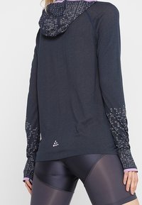 Námořnická sportovní mikina s vzorovanou kapucí, dlouhými rukávy se pixelovými detaily a přiléhavým střihem. Materiál se zdá být lehký a strukturovaný.