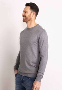 Grijze ronde hals sweater van een zachte brei, getailleerde silhoutte, met geribbelde manchetten en zoom, gecombineerd met blauwe spijkerbroek.