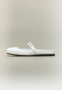 Άσπρο επίπεδο παπούτσι με στρογγυλεμένη μύτη και λεπτό λουράκι στον αστράγαλο. Λείο συνθετικό υλικό με σκούρα σόλα και διακριτική λεπτομέρεια ραφής.