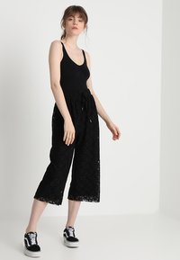 Čierne čipkované culottes s uvoľneným strihom, s elastickým pásom a širokými nohavicami, kombinované s priliehavým čiernym tielkom a teniskami.