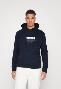 Felpa con cappuccio blu navy, dotata di tasca anteriore e patch logo bianco. Presenta lacci, polsini a costine e una texture morbida.