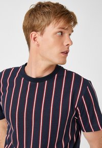 Camiseta de color azul marino con rayas verticales rojas y blancas, de manga corta y escote redondo. Tejido de mezcla de algodón con una textura suave.