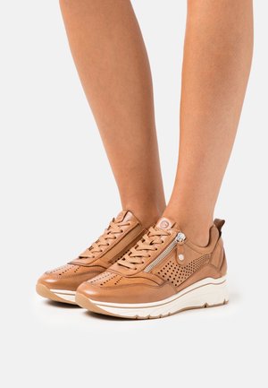 Hellbraune Ledersneaker mit perforiertem Design, Schnürsenkeln und seitlichem Reißverschluss. Weiße, gepolsterte Sohle. Glatte Textur und abgerundete Form.