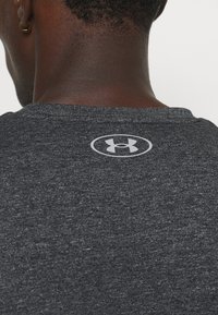 Šedé vřesové tričko s krátkým rukávem vyrobené z měkké látky; má malou odrazovou značku Under Armour na zadní straně krku.