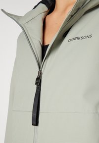 Giacca zip-up verde chiaro con colletto alto e dettagli neri, dotata di un interno texturizzato e branding sul petto.