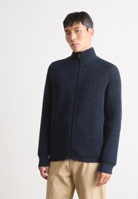 Cárdigan de punto acanalado en color marino con cuello alto, cremallera completa y mangas largas. Hecho de un material suave y texturizado.