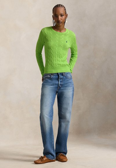 Πράσινο πλεκτό πουλόβερ με πλεξούδα, μπλε τζιν παντελόνι ίσιας γραμμής και καφέ μοκασίνια. Το πουλόβερ έχει στρογγυλή λαιμόκοψη και ριμπ μανσέτες.