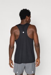 Μαύρη αθλητική αμάνικη μπλούζα με ραβδωτή υφή, φαρδιά μανίκια και κυκλική λεπτομέρεια. Φοριέται με γκρίζες βερμούδες με λευκές λεπτομέρειες.