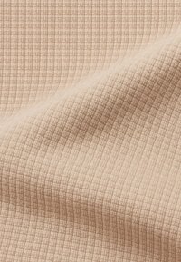 Lichtbeige stof met een gestructureerd, ruitpatroon. Het oppervlak lijkt geweven en zacht, met subtiele verticale lijnen.