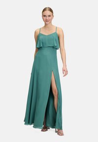 Robe maxi teal avec une couche supérieure évasée et des fines bretelles, dotée d'une fente sur le côté, fabriquée en tissu lisse, pour une silhouette fluide.