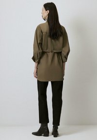 Cămașă supradimensionată verde măslin cu mâneci lungi și talie strânsă, combinată cu pantaloni negri slim-fit și cizme negre până la gleznă.
