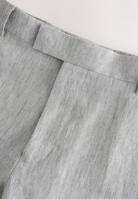 Gros plan de la taille d'un pantalon en lin gris clair avec passants de ceinture et détails de plis à l'avant.