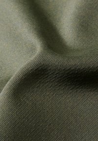 Texturiertes Gewebe in Olivgrün mit einem subtilen gerippten Muster. Das Material wirkt weich und leicht glänzend, mit sanften Falten.