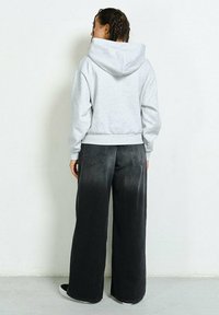 Gray sweatshirt with a hood, paired with black wide-leg jeans. The fabric appears soft, with a smooth texture and ribbed cuffs.