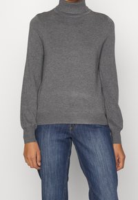 Pull à col roulé gris à manches longues, texture en maille douce, poignets et ourlet côtelés, accompagné de jean en denim. Design simple et classique.