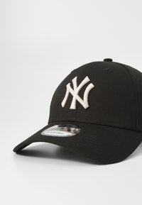 Schwarze Baseballmütze aus Stoff mit verstellbarem Riemen. Sie hat ein auffälliges, weiß gesticktes Logo auf der Vorderseite und einen strukturierten Schirm.