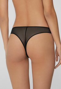 Schwarzer, durchsichtiger Mesh-String mit glatter Textur, minimaler Bedeckung und schlichtem Design. Dezente Nahtdetails entlang der Kanten.