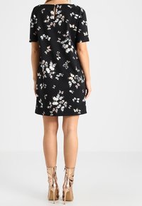 Vestido negro de manga corta con un patrón floral en rosa y blanco, que presenta un detalle de ojal en la parte posterior. La modelo lleva botas metálicas hasta los tobillos.