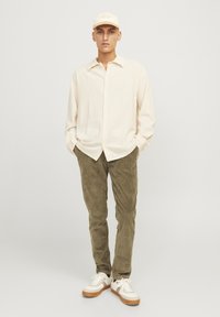 Light beige button-up shirt with a textured surface; olive green corduroy pants; white sneakers with a light brown sole; beige cap.