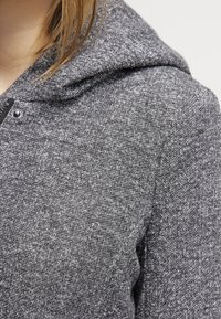 Felpa con cappuccio grigia in tessuto strutturato, con cappuccio regolabile da coulisse e dettaglio con cerniera al collo. Aspetto morbido e caldo.