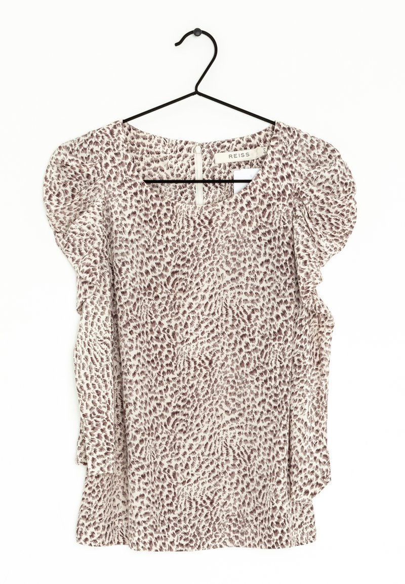 Blouse légère avec des manches bouffantes, présentant un fond beige et un imprimé animalier abstrait en brun. Col rond, fermeture éclair au dos.