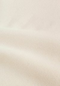 Tissu en coton de couleur blanc cassé, présentant une surface finement texturée avec de légères nervures et de petites taches, doux et souple.