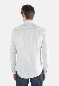 Camicia bianca a maniche lunghe con un sottile motivo geometrico in blu e rosso. Caratterizzata da un colletto standard e polsini con bottoni, abbinata a jeans blu.