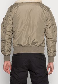 Giubbotto bomber color khaki con colletto in pelliccia sintetica, polsini e orlo a costine, e texture trapuntata; presenta cuciture laterali e spalle leggermente imbottite.