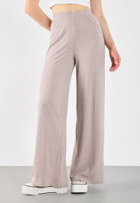 Pantaloni a gamba larga ribattuti color rosa chiaro con vita alta. Il tessuto sembra morbido con una finitura texture. Indossati con sneakers bianche con piattaforma.