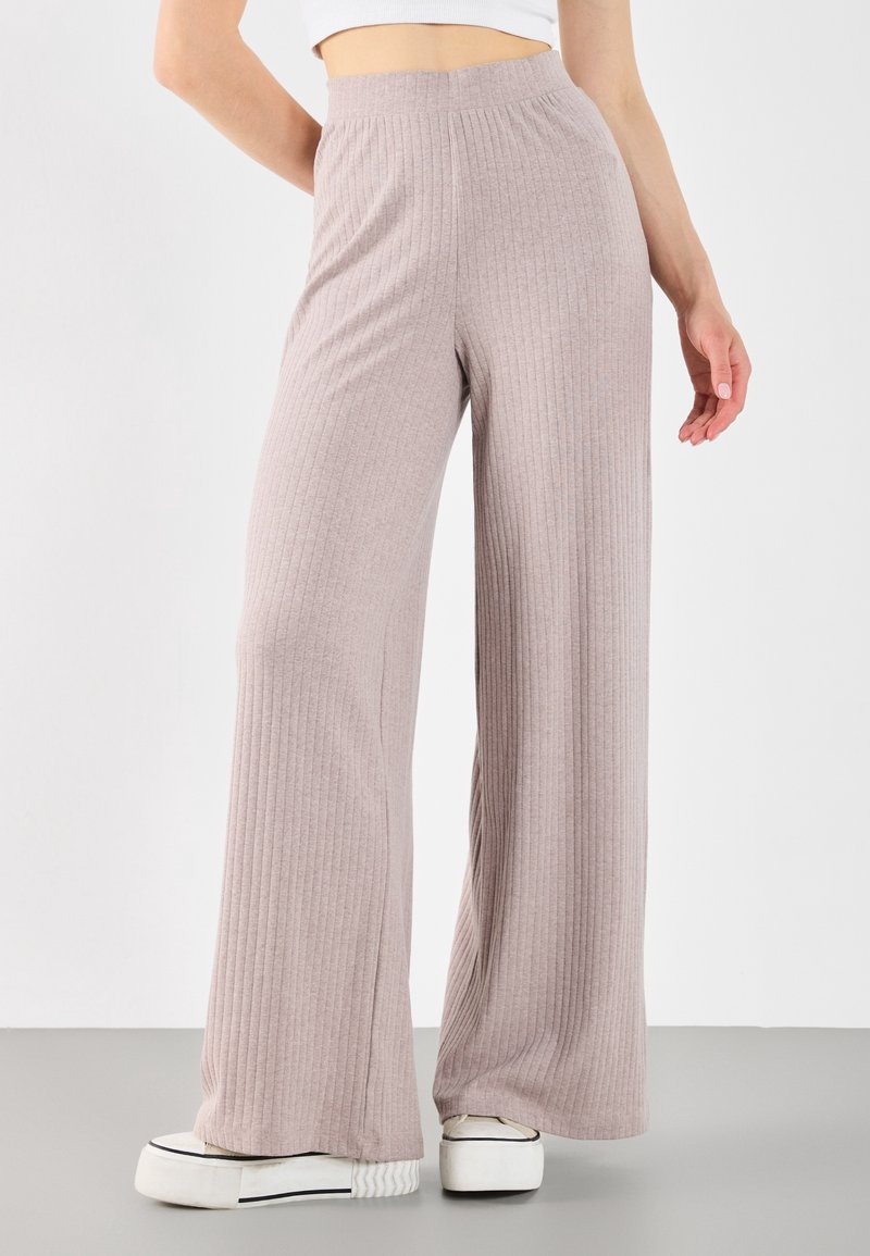 Pantaloni a gamba larga ribattuti color rosa chiaro con vita alta. Il tessuto sembra morbido con una finitura texture. Indossati con sneakers bianche con piattaforma.
