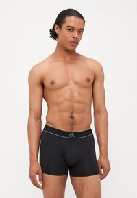 Schwarze Boxershorts aus glattem, dehnbarem Material, mit einem markierten elastischen Bund in Grau und einem konturierten Taschen-Design.