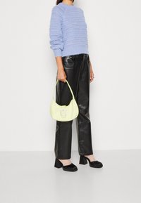 Maglione blu lavorato a maglia con strisce texture, pantaloni in ecopelle neri e una borsa a spalla verde chiaro con una fibbia decorativa. Scarpe nere con tacco a blocco.