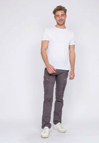 Pantalons cargo gris avec plusieurs poches latérales, associés à un t-shirt blanc classique et des baskets blanches. Design simple et fonctionnel.