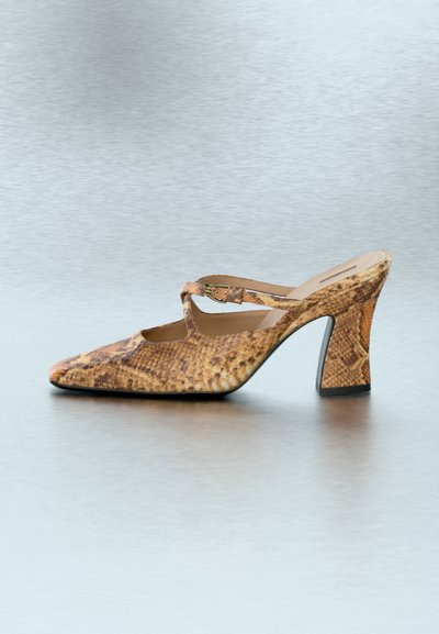 Καφέ mule με σχέδιο φίδι στο πέλμα, ψηλό τακούνι, τετράγωνη μύτη και λεπτό λουράκι με αγκράφα πάνω από τον ταρσό σε γκρι επιφάνεια.