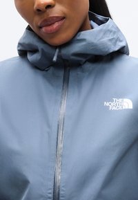 Ελαφρύ, ανοιξιάτικο μπουφάν με κουκούλα σε απαλό μπλε χρώμα, με κεντρικό φερμουάρ και εμφανές λευκό λογότυπο στο αριστερό στήθος. Λεία, ματ υφή.