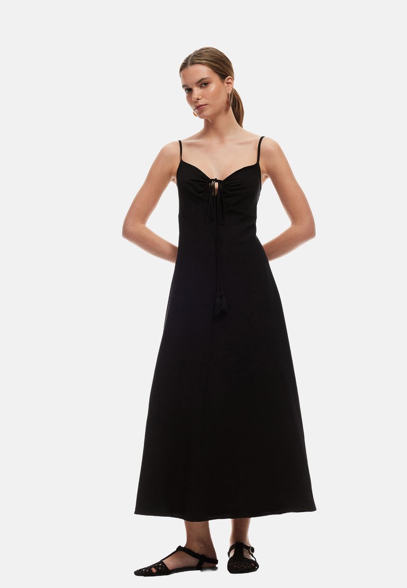 Zwarte maxi-jurk met spaghettibandjes, een strikdetail aan de voorkant en een franjesaccent. Glad materiaal met een aangesloten bovenstuk en een vloeiende rok.
