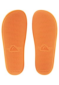 Oransje flip-flop såler med en teksturert bølgeformet mønster for grep, med en logoavtrykk på hælen og myk gummi.