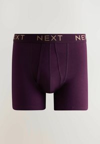 Purpuriniai bokso šortai iš glotnaus, tampraus audinio. Juosmuo su auksiniu, kontrastuojančiu „NEXT“ logotipu ant elastinės juostos.