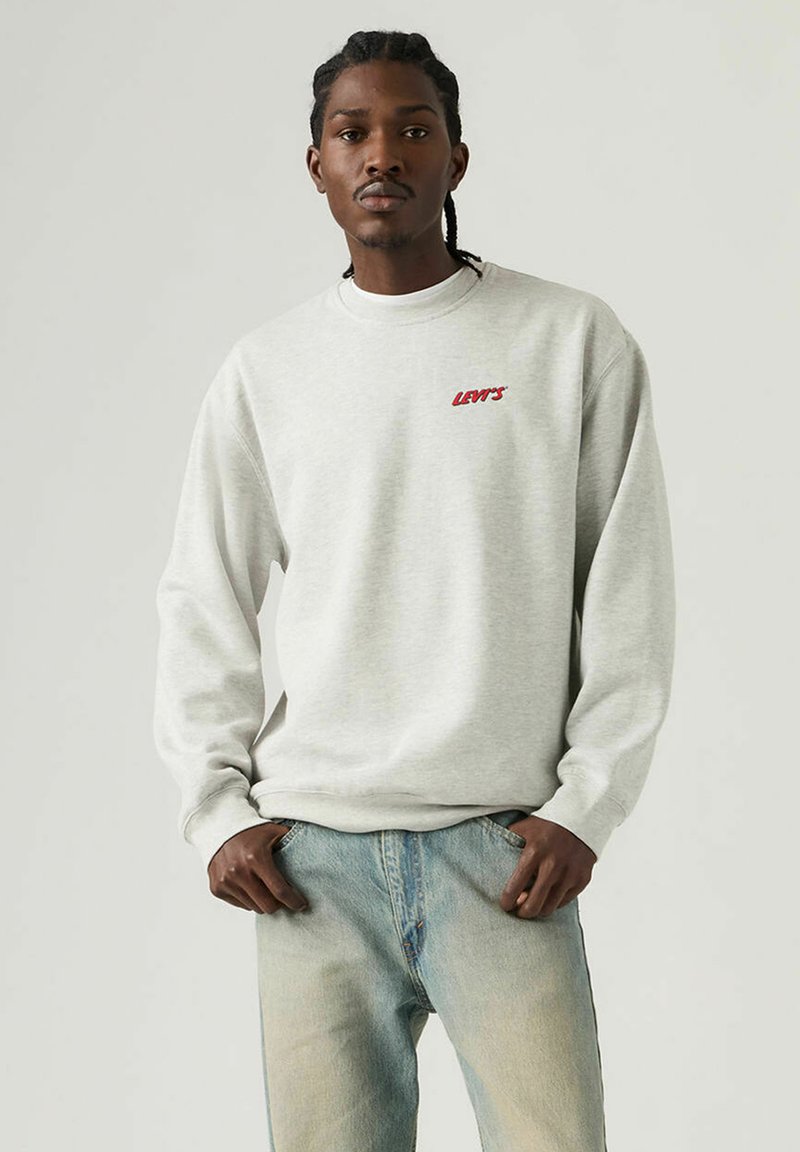 Sweat-shirt gris à manches longues avec poignets côtelés. Présente un logo "LEVI'S" rouge sur la poitrine. Associé à un jean bleu délavé.