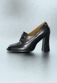 Μαύρο δερμάτινο παπούτσι με ψηλό τακούνι, στρογγυλεμένη μύτη, κλείσιμο με κορδόνια, χρυσά ρούχια και φαρδύ τετράγωνο τακούνι πάνω σε ομαλή γκρι επιφάνεια.