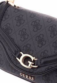 Borsa Guess nera in tessuto con texture, dotata di chiusura e logo "G" dorati, caratterizzata da un motivo a rilievo ripetuto sul materiale.