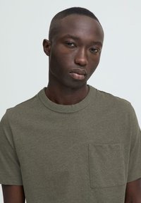 Pametna zelena majica od pamuka s okruglim izrezom, kratkim rukavima i džepom na prsima. Mekana tekstura i ležerni kroj.