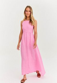 Maxi sukienka w jasnoróżowym kolorze, uszyta z lekkiego materiału, posiada dopasowaną górę i zwiewny dół. Modelka nosi brązowe sandały na paski.