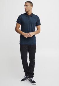 Marine gestreiftes Poloshirt mit flachem Kragen und kurzen Ärmeln, kombiniert mit schwarzen Slim-Fit-Hosen und schwarzen Sneakers mit weißen Akzenten.