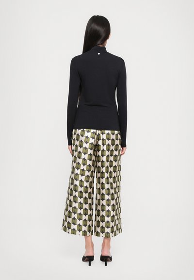 Zwarte fitted turtleneck shirt gecombineerd met gestreepte groene en crèmekleurige wijde broek met geometrische vormen en zwarte accenten.