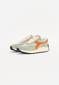 Green suede sneakers with orange accents, cream laces, and a black rubber sole. Features a retro design and contrasting stitching details.