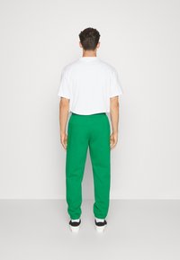 Grønne sweatpants med elastiske manchetter og talje, parret med en hvid t-shirt med korte ærmer, set bagfra.