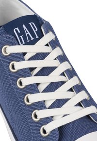 Zapatillas de lona azules con cordones y ojales blancos, con una lengüeta color marino que muestra "GAP" en texto blanco y tela texturizada.